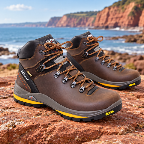 Brown Grisport walking boots on red sandstone with the South Devon coast behind