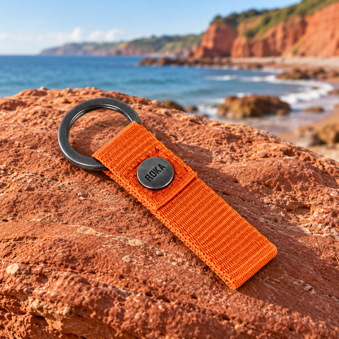 Orange Roka fabric keyring on a red sandstone rock beside a South Devon beach